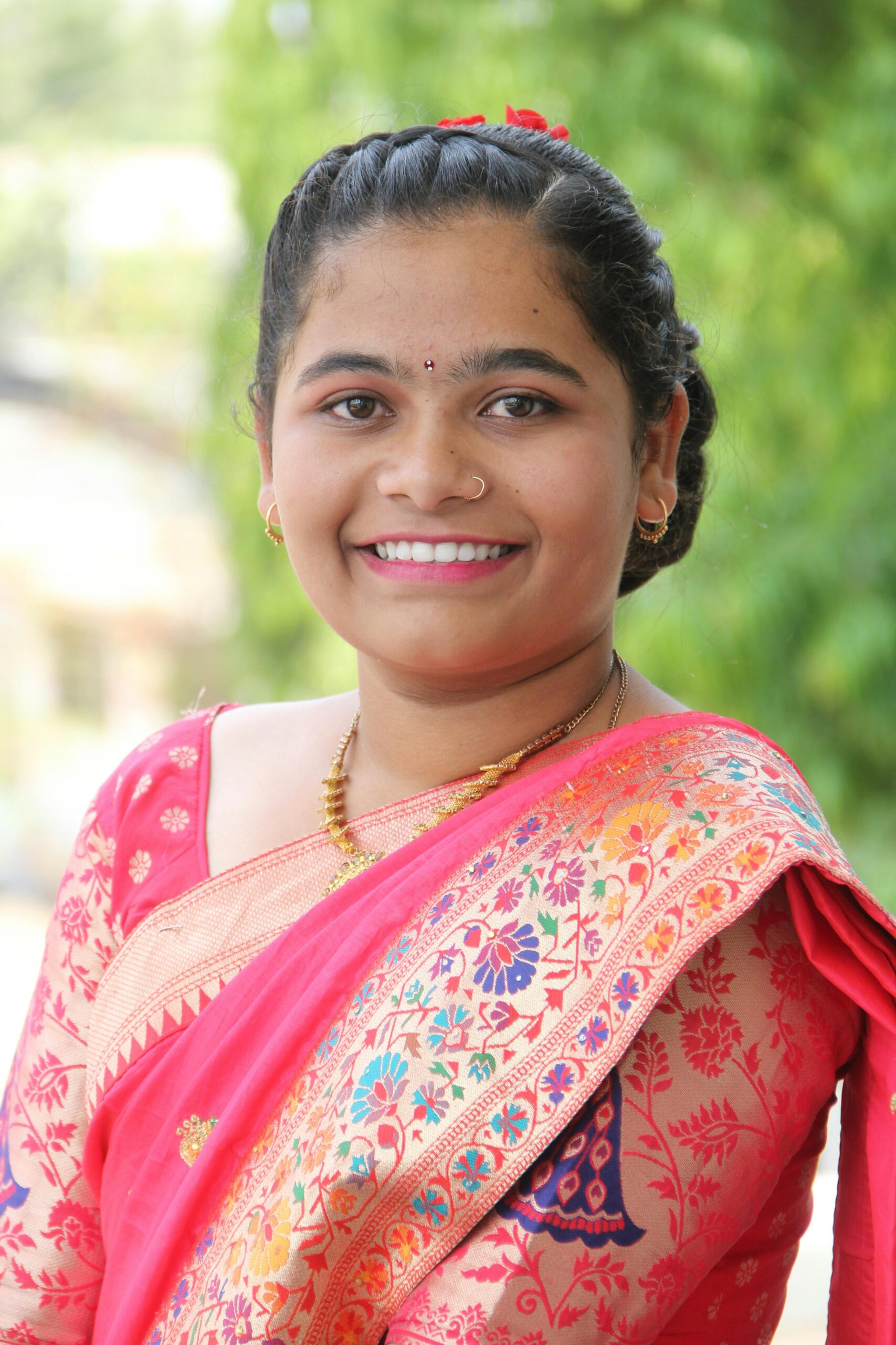 A cheerful woman in traditional Indian attire posing outside with a bright smile.